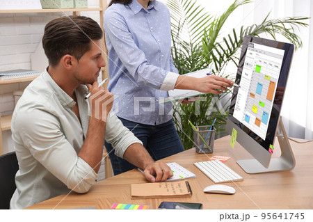 Colleagues working with calendar app on computer in office Colleagues working with calendar app on computer in office 95641745