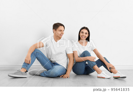 Young couple in stylish jeans sitting near white wall Young couple in stylish jeans sitting near white wall 95641835