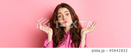 Close up portrait of clueless woman looking coy and unaware, shrugging shoulders, know nothing, cant understand, standing over pink background Close up portrait of clueless woman looking coy and unaware, shrugging shoulders, know nothing, cant understand, standing over pink background 95642832