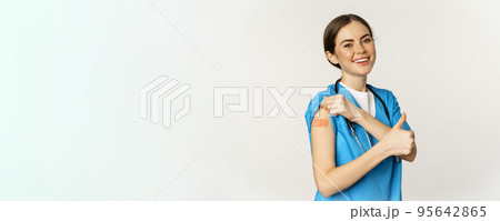 Happy smiling medical worker, doctor or nurse showing her shoulder after vaccination, covid-19 vaccine and thumbs up satisfied, standing over white background Happy smiling medical worker, doctor or nurse showing her shoulder after vaccination, covid-19 vaccine and thumbs up satisfied, standing over white background 95642865