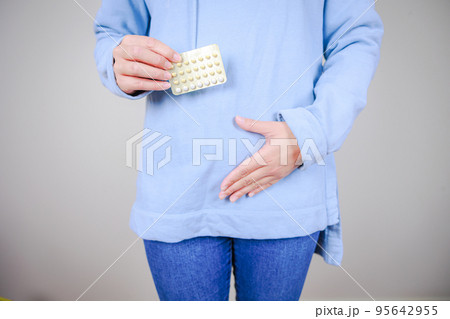 経口避妊薬（低用量ピル）を持ちお腹をさする女性	 95642955