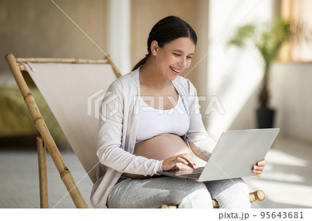 Portrait Of Happy Young Pregnant Woman Relaxing In Chair With Laptop 95643681