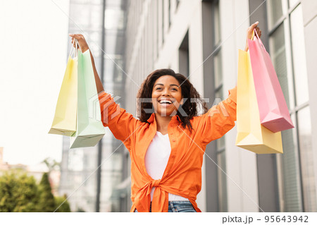 Happy excited pretty millennial african american lady in casual with open mouth with many bags, rising hands up 95643942