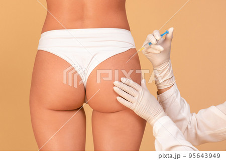 Butt lifting concept. Back view of plastic surgeon making injection at buttocks area for young lady, closeup 95643949
