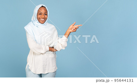 Look there. Happy black muslim lady pointing finger aside at copy space over blue background, showing place for your ad 95644131
