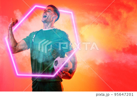 Caucasian male player with soccer ball screaming over illuminated hexagon against neon background Caucasian male player with soccer ball screaming over illuminated hexagon against neon background 95647201