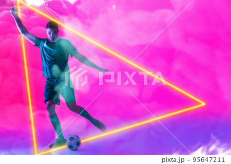 Caucasian male player playing with ball over illuminated triangle against pink neon background 95647211