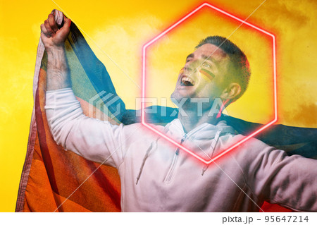 Male caucasian player with german flag screaming over illuminated hexagon against yellow background 95647214
