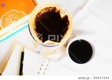 白いテーブルの上のハンドドリップコーヒーと手帳、ペン、本 95647334