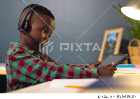 Smiling african american boy learning, using headphones and tablet with copy space at home Smiling african american boy learning, using headphones and tablet with copy space at home 95648687
