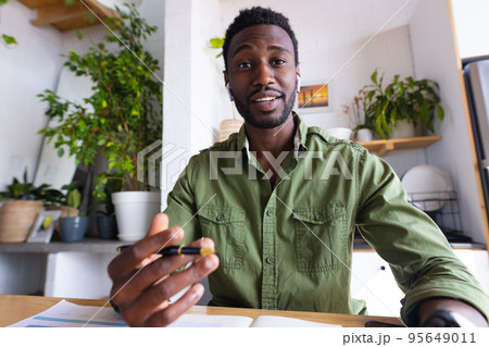 Happy african american man sitting at table in kitchen, having video call 95649011