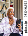 Happy african american woman wearing santa claus hat, using smartphone for video call 95649852