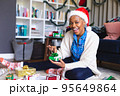Happy african american woman wearing santa claus hat, packing presents 95649864