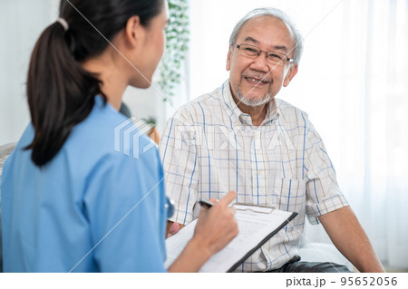 Young female doctor inquires personal data of a contented senior at home. 95652056