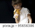 young boy is eating banana on black background. Diet and fruits. 95656386
