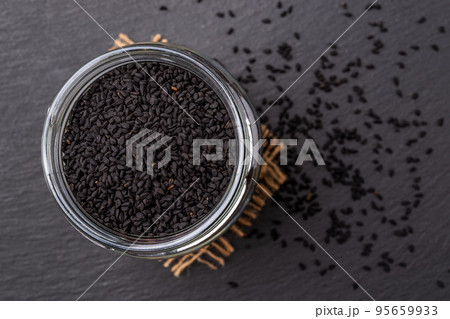 Glass jar full of black cumin seeds over black background. Glass jar full of black cumin seeds over black background. 95659933