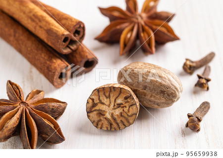 Whole and halved nutmeg seeds, cinnamon sticks, few cloves, and star anise on a wooden background. 95659938