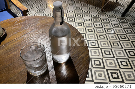 Selective focus, A clear glass filled with ice and clear glass bottle holds cold mineral water sits on wooden table, water use to quench thirst 95660271