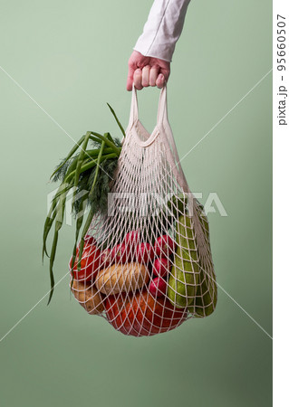 Mesh bag with vegetables and herbs in female hand. Mesh bag with vegetables and herbs in female hand. 95660507
