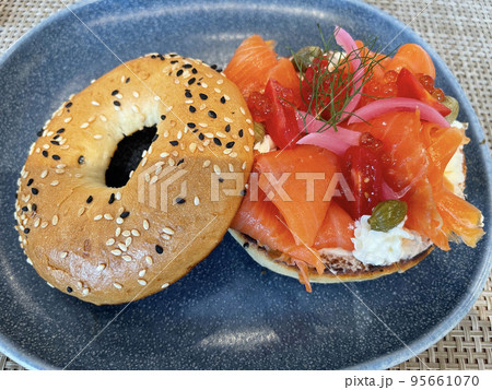 Selective focus, delicious bagel with smoked salmon, spinach, red onions, tomatoes, avocado and cream cheese over a blue plate background. Selective focus with slight blurred parts 95661070