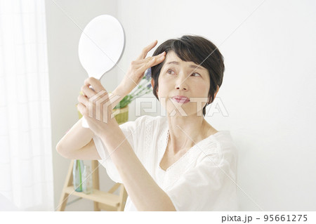 自宅で鏡を見て髪の毛をチェックする中年女性 95661275