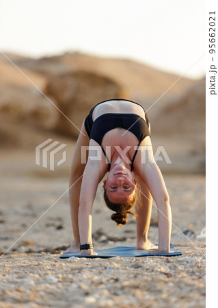 Young woman doing wheel yoga pose at the beach in the evening 95662021