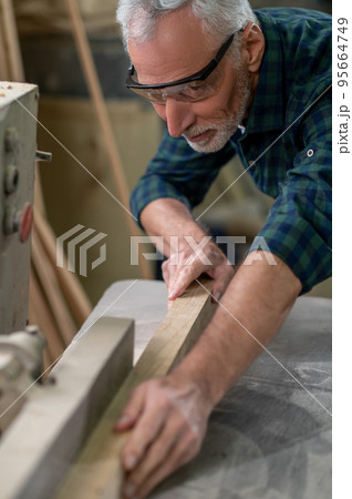 Mature carpenter working in a worshop and looking involved Mature carpenter working in a worshop and looking involved 95664749