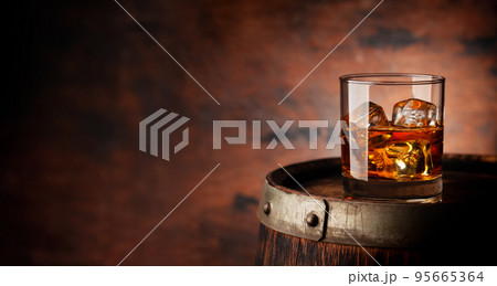 Glass of whiskey with ice cubes on the old barrel 95665364