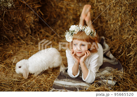 A cute and beautiful little girl is sitting in the hayloft with a rabbit 95665520