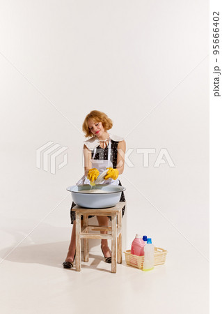Portrait of stylish woman in dress and apron washing the dishes in foamy bowl isolated on white background 95666402