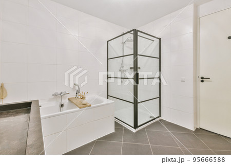 Sinks with mirrors and clean bathtub located near shower box with glass door in modern bathroom with white tiled walls 95666588
