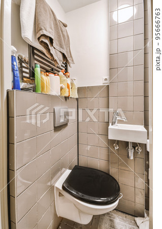 Interior of narrow restroom with sink and wall hung toilet with white walls and checkered floor Interior of narrow restroom with sink and wall hung toilet with white walls and checkered floor 95666763