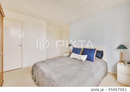 Home interior design of bedroom with bed and wooden wardrobe placed in corner near window in modern apartment 95667061