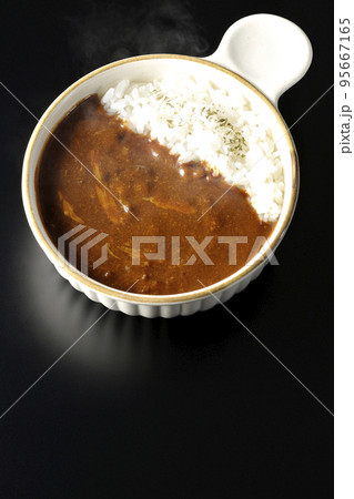 耐熱皿に盛られた熱々チーズカレーライスを黒背景で俯瞰撮影 95667165