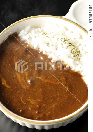 耐熱皿に盛られた熱々チーズカレーライスを黒背景で俯瞰撮影 95667166