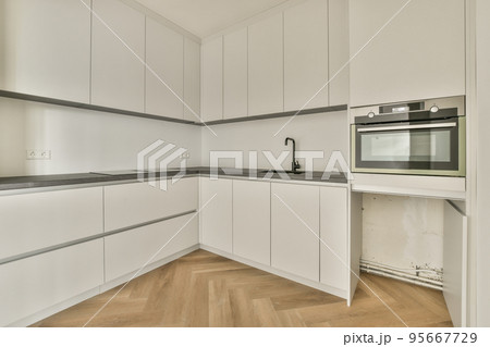 Interior of light kitchen with cupboards and appliances located in flat at daytime Interior of light kitchen with cupboards and appliances located in flat at daytime 95667729