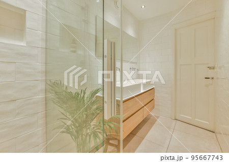 Fragment of interior of modern white bathroom with wooden cabinet under sink and with mirror and towel 95667743