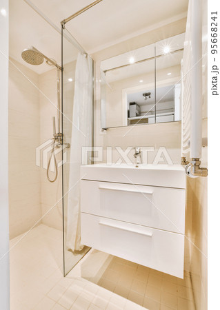 Sinks with mirrors and shower box with glass door in modern bathroom with white tiled walls Sinks with mirrors and shower box with glass door in modern bathroom with white tiled walls 95668241