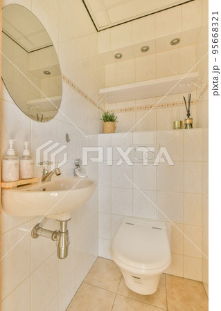 Interior of narrow restroom with sink and wall hung toilet with white walls and checkered floor Interior of narrow restroom with sink and wall hung toilet with white walls and checkered floor 95668321