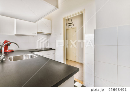 Well organized small home kitchen interior with sink under window and light furniture with stove and fridge in urban apartment 95668491