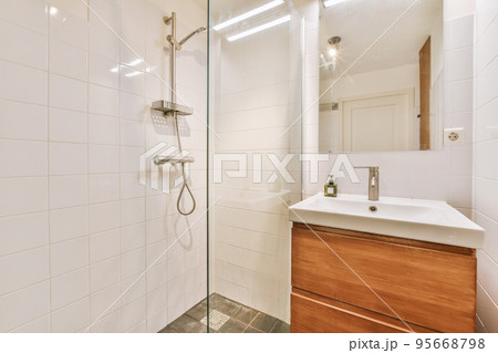 Sinks with mirrors and shower box with glass door in modern bathroom with white tiled walls Sinks with mirrors and shower box with glass door in modern bathroom with white tiled walls 95668798