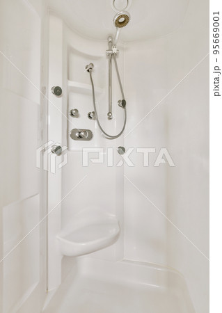 Shower faucets attached to tiled wall near glass partition and ornamental curtail in washroom at home Shower faucets attached to tiled wall near glass partition and ornamental curtail in washroom at home 95669001