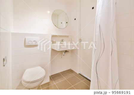 Bathroom with white tiled walls and open shower near sink and toilet in light Bathroom with white tiled walls and open shower near sink and toilet in light 95669191