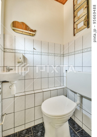Wall hung toilet and small sink in corner in lavatory room with beige tile Wall hung toilet and small sink in corner in lavatory room with beige tile 95669488