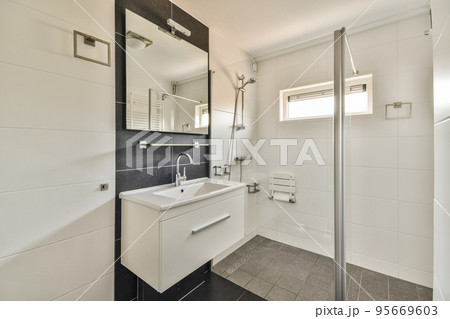 Stylish interior design of small bathroom with white walls and shelves and with large mirror near sink illuminated with lamps 95669603