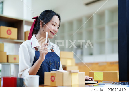 Starting small business entrepreneur of independent Asian woman smiling using computer laptop with cheerful success of online marketing package box items and SME delivery concept. 95671810