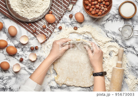 Close-up shot. Top view of a baker cook place, hands are working with a raw dough on the marble table background. Close-up shot. Top view of a baker cook place, hands are working with a raw dough on the marble table background. 95673003
