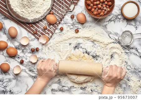 Close-up shot. Top view of a baker cook place, hands are working with a raw dough on the marble table background. Close-up shot. Top view of a baker cook place, hands are working with a raw dough on the marble table background. 95673007
