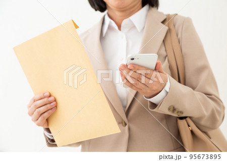 書類の入った封筒とスマホを持つミドル女性のビジネスウーマン 95673895