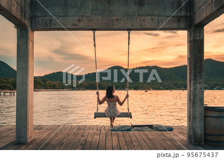 Young asian woman sitting and enjoying on wooden swing in tropical sea at the evening 95675437